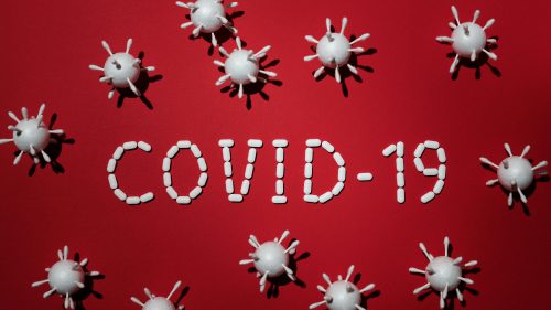Creative depiction of COVID-19 using pills and virus models on a red backdrop.